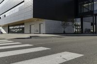 some people are walking across a crosswalk near a large building while two zebra crossing crosses are near