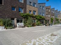 a building on a quiet street with plants in front of it and cars parked on the road