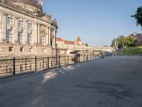 there is a large building near the water in the city park, it has a pedestrian bridge