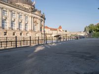 there is a large building near the water in the city park, it has a pedestrian bridge