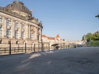 there is a large building near the water in the city park, it has a pedestrian bridge