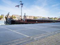 a barge boat is next to a street with buildings in the background at a marina