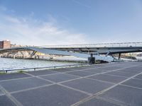 a road leading to a bridge over water surrounded by large buildings with a sky in the background