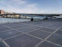 a road leading to a bridge over water surrounded by large buildings with a sky in the background