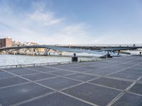 a road leading to a bridge over water surrounded by large buildings with a sky in the background