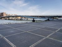 a road leading to a bridge over water surrounded by large buildings with a sky in the background