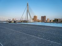 a pedestrian bridge over a river on a sunny day in europe by a city skyline