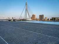 a pedestrian bridge over a river on a sunny day in europe by a city skyline