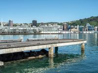 a pier stretches across a body of water near a cityscape and mountains in the distance