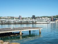 a pier stretches across a body of water near a cityscape and mountains in the distance