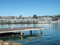 a pier stretches across a body of water near a cityscape and mountains in the distance