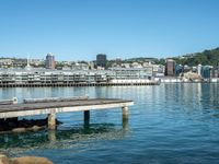 a pier stretches across a body of water near a cityscape and mountains in the distance