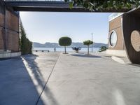 a cement walkway that leads into a parking garage with two trees and a large potted tree