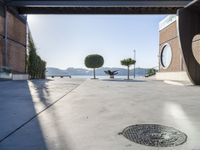 a cement walkway that leads into a parking garage with two trees and a large potted tree