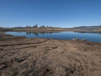 the dirt is near a water body with hills in the background and blue sky overhead