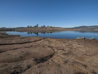 the dirt is near a water body with hills in the background and blue sky overhead