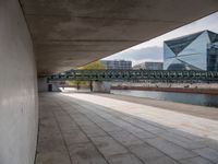 walkway beside a river under an overpass in a city with skyscrapers and sky