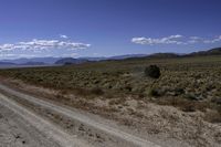 an empty dirt road with mountains in the distance against a clear blue sky at one end