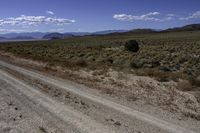 an empty dirt road with mountains in the distance against a clear blue sky at one end