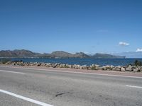 a deserted highway with some rocks near the water and mountains in the distance and an ocean in front