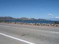 a deserted highway with some rocks near the water and mountains in the distance and an ocean in front