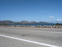 a deserted highway with some rocks near the water and mountains in the distance and an ocean in front