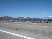 a deserted highway with some rocks near the water and mountains in the distance and an ocean in front