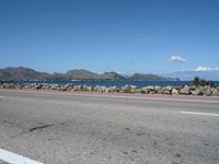 a deserted highway with some rocks near the water and mountains in the distance and an ocean in front