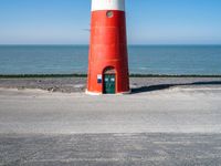 the lighthouse is bright red and white near the ocean water a black bench can be seen