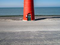 the lighthouse is bright red and white near the ocean water a black bench can be seen