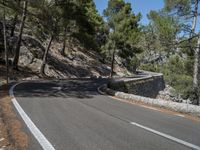 a motorcycle is going along the side of the mountain road with a rock wall separating the road