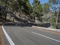 a motorcycle is going along the side of the mountain road with a rock wall separating the road