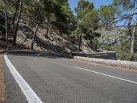 a motorcycle is going along the side of the mountain road with a rock wall separating the road