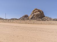 a truck driving through the desert with large rocks in the background of it and power lines