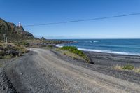 a gravel road going past the ocean on the edge of a cliff face at low tide