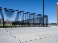 a cement floor area with an empty lot behind it and a fence surrounding the park