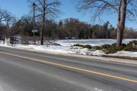 a road with snow and trees next to a street sign and a field of snow