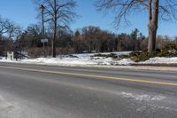 a road with snow and trees next to a street sign and a field of snow