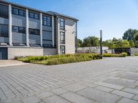 empty concrete parking lot with large buildings in back ground area of outdoor space next to tall grass and shrubs