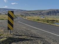 a black and yellow striped sign by the side of a road with mountains in the background