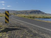 a black and yellow striped sign by the side of a road with mountains in the background