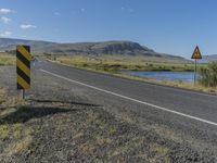 a black and yellow striped sign by the side of a road with mountains in the background