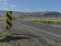 a black and yellow striped sign by the side of a road with mountains in the background