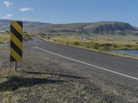 a black and yellow striped sign by the side of a road with mountains in the background