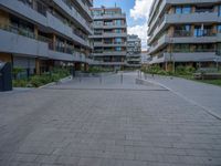 a skateboarder riding through the middle of an open concrete courtyard with buildings in the background