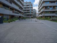 a skateboarder riding through the middle of an open concrete courtyard with buildings in the background