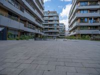 a skateboarder riding through the middle of an open concrete courtyard with buildings in the background