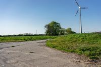 the road leads down to an empty farm field with wind turbines on the horizon in front of it