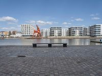 an empty bench sitting on the side of a river with buildings in the background and water behind