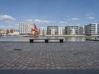 an empty bench sitting on the side of a river with buildings in the background and water behind